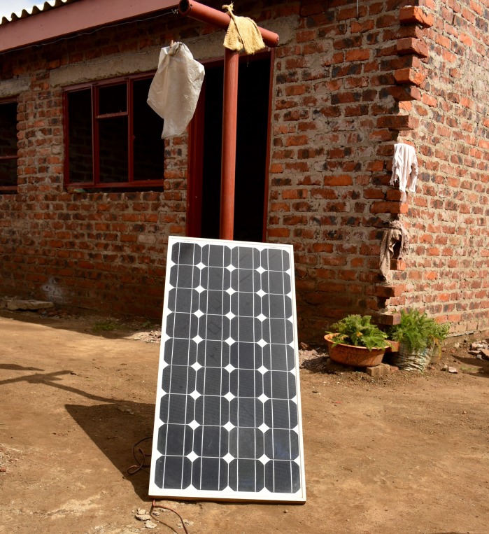 A full-sized “roof” solar panel leaning up against a clothesline. Often roof-mounting panels is structurally challenging, so it is not uncommon to see these larger panels placed nearby on the ground.