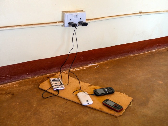 It is not uncommon to see one outlet shared by many members of a community. This outlet is in the community center, which is one of a small number of grid-connected structures. Note the variety of feature phones.